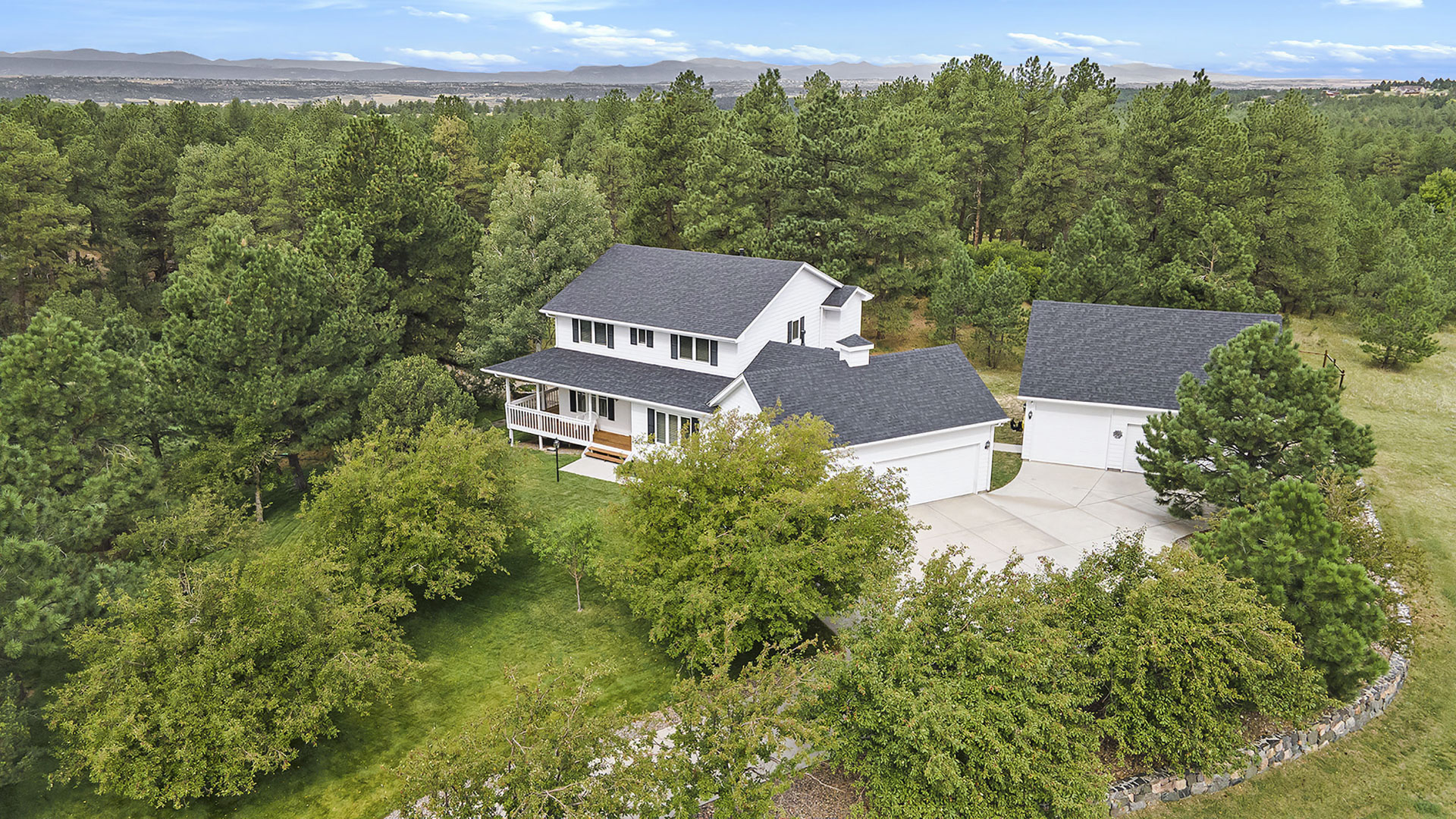 High-quality aerial drone image of a luxury two-story home surrounded by abundant trees on a 2-acre property.