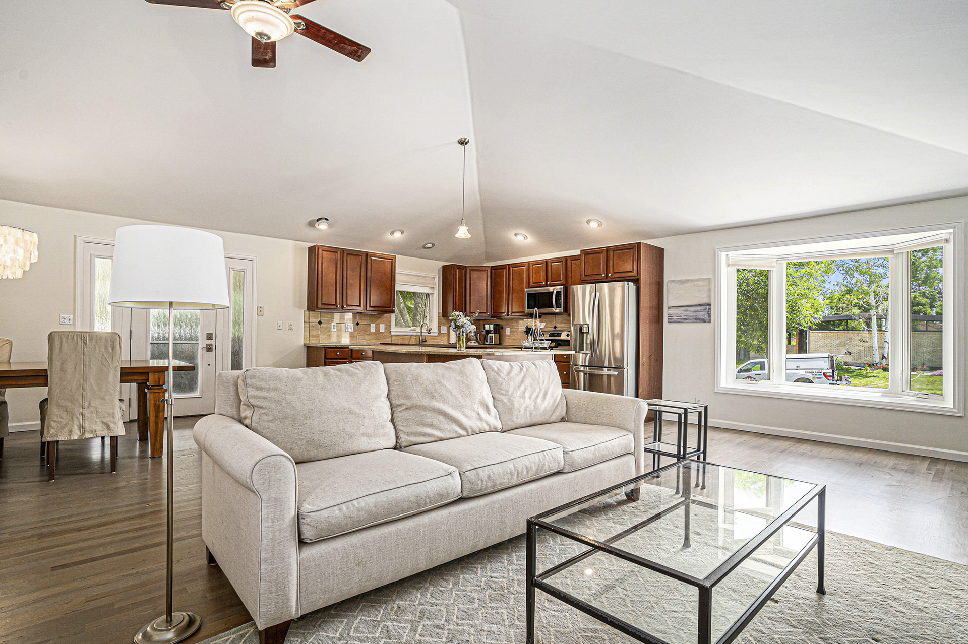 Living room and kitchen with vaulted ceilings, a large picture window, and wood floors.