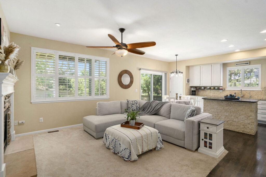 Living room with a fireplace, ceiling fan, and carpet, overlooking an updated kitchen and a walk-out balcony.
