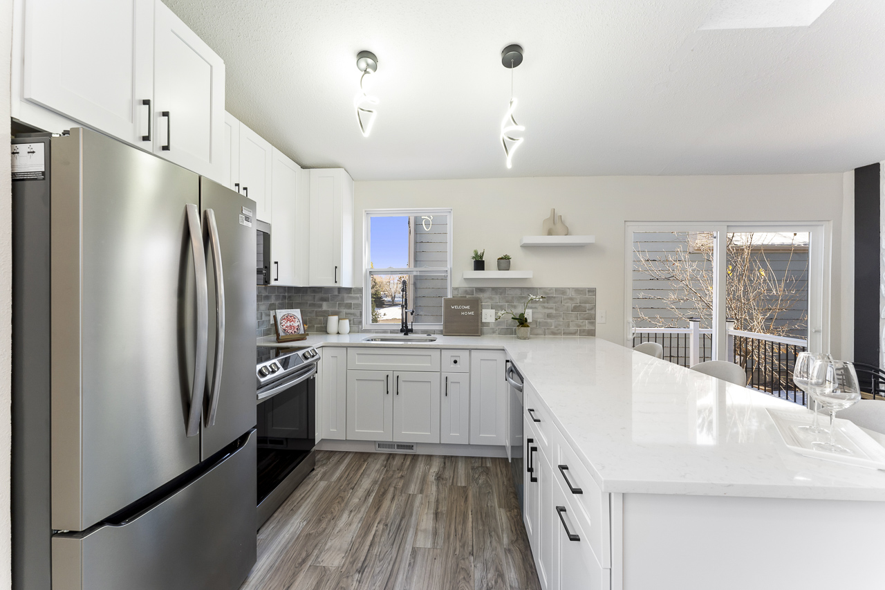 Newly renovated kitchen with stainless steel appliances, white quartz countertops, new cabinets, and modern lighting fixtures.